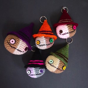 May include: Five crocheted Halloween-themed keyrings with different coloured hats and button eyes. The keyrings are brown, tan, green, purple and orange.