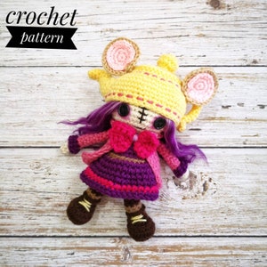 May include: A handmade crochet doll wearing a yellow hat with mouse ears, a pink bow, and a purple dress. The doll has black button eyes and purple hair. The text "crochet pattern" is in the upper left corner.