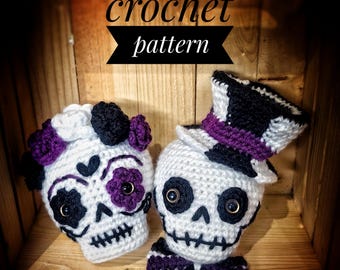 May include: Crochet pattern for a pair of sugar skull amigurumi. The female skull has a white flower and purple flowers on her head. The male skull has a black top hat with a purple band. Both skulls have black eyes and purple accents.