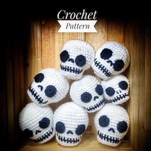 Può includere: Un gruppo di otto teschi in crochet bianco con occhi e bocche neri. I teschi sono disposti in cerchio su una superficie di legno. Modello di uncinetto.