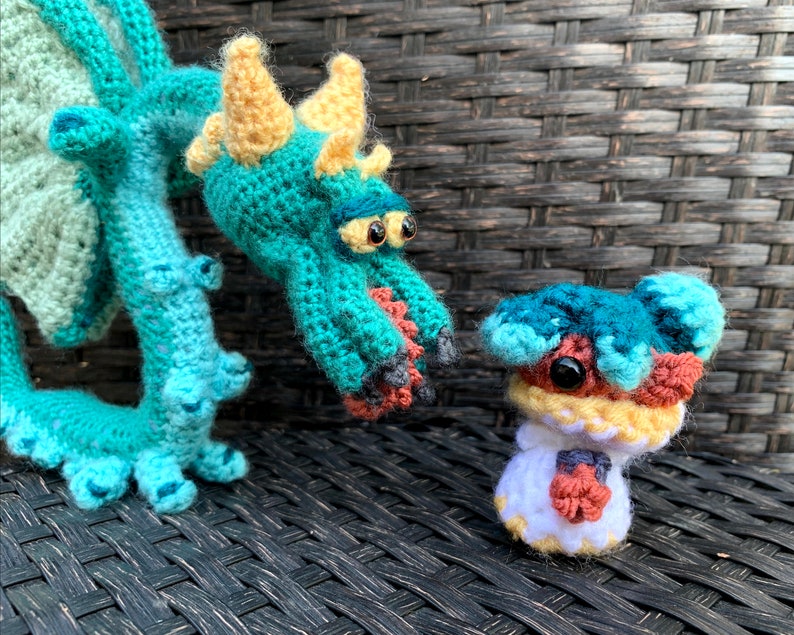 May include: A teal crocheted dragon with yellow horns and a small teal crocheted creature with brown and yellow accents.