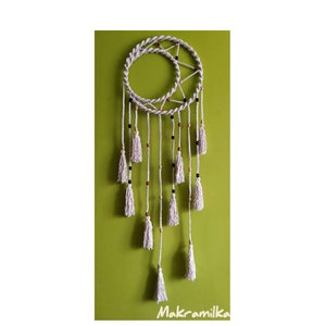 Op de afbeelding: Een witte macramé droomvanger met een halve maan ontwerp en houten kralen. De droomvanger heeft witte kwastjes die aan de onderkant hangen.