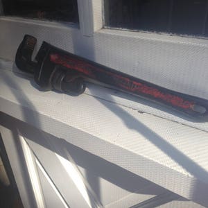 May include: A black adjustable wrench with a red painted handle. The wrench is lying on a white surface.