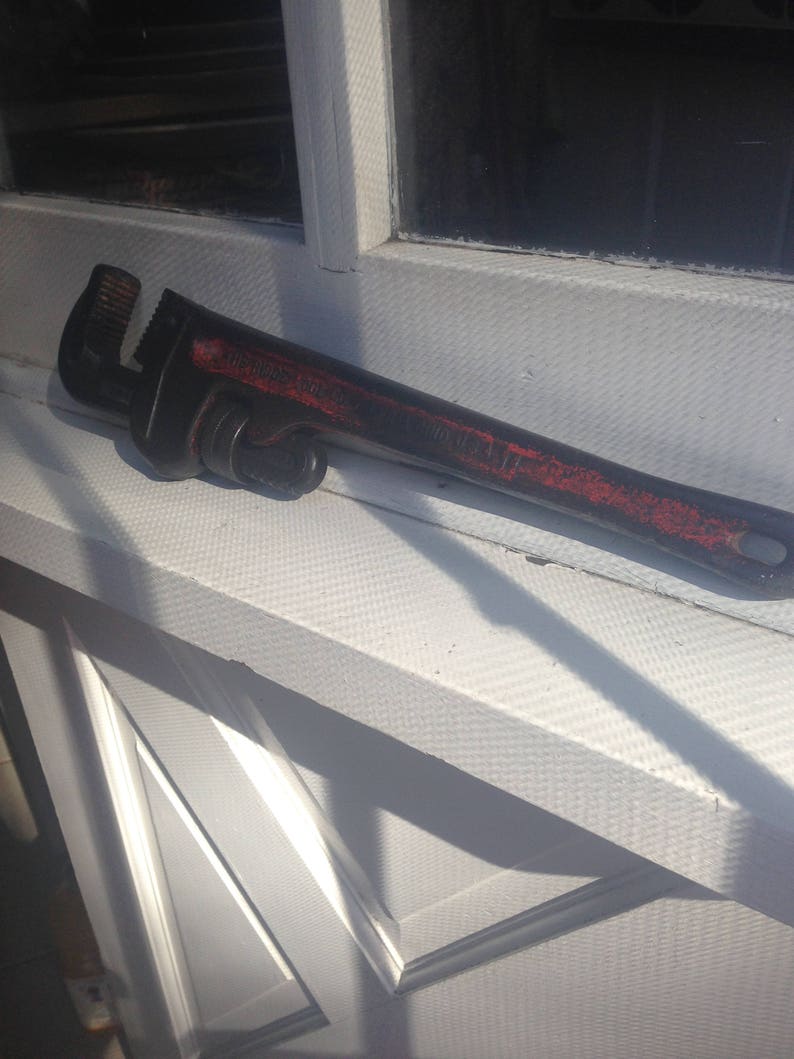 May include: A black adjustable wrench with a red painted handle. The wrench is lying on a white surface.