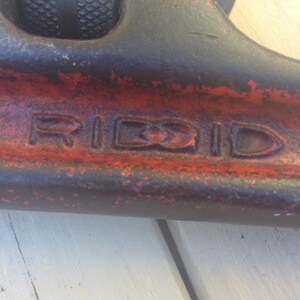 May include: Close-up of a red and black pipe wrench with the word "RIDGID" embossed on the side.
