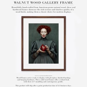 Framed artwork of Cinder in a walnut wood frame with white matte, showcasing a Victorian-style portrait of a woman in a dark dress holding a deep red heart-shaped vessel.