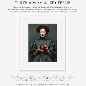 Fine art print of Cinder framed in a white wood frame with matte, highlighting a red-haired woman in vintage attire holding a sculpted heart on a moody green background.