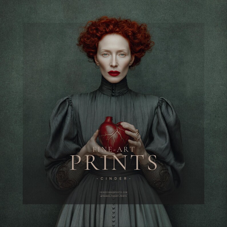 Woman in vintage dark gray pleated gown with red hair and bold red lipstick holding a red anatomical heart-shaped vessel, posed against a painterly green-gray background.
