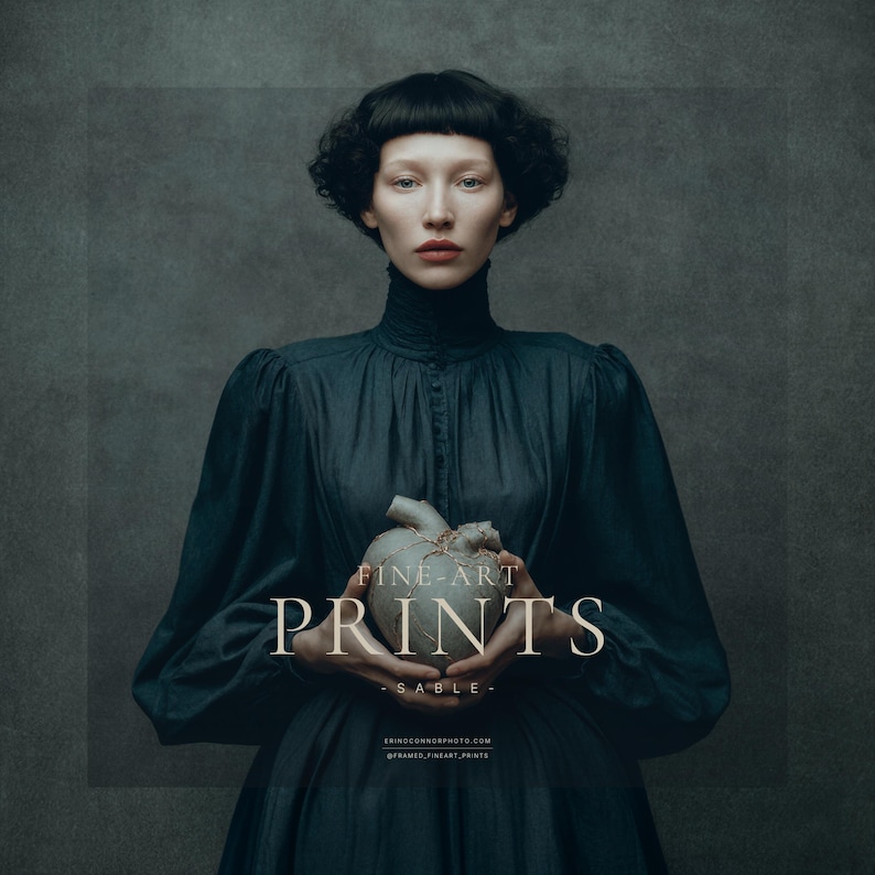 Fine art portrait of a woman named Sable holding a gray ceramic heart with gold kintsugi cracks, wearing a dark high-necked dress on a painterly textured background.