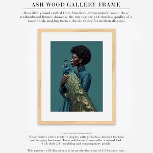 Puede incluir: Marco de galer&iacute;a de madera de fresno con acabado de madera natural. El marco rodea una impresi&oacute;n de color verde azulado de una persona sosteniendo un pavo real. El texto "ASH WOOD GALLERY FRAME" est&aacute; en la parte superior.