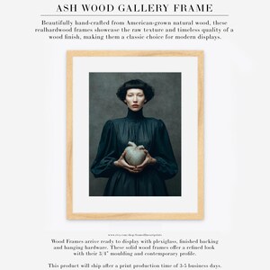 Sable framed in an ash wood gallery frame with white matte, featuring a dark-haired woman holding a gold-repaired heart on a moody green backdrop.