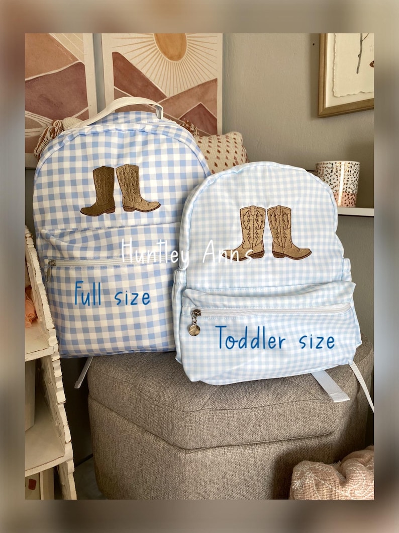 Puede incluir: Dos mochilas de cuadros vichy azul claro, una de tama&ntilde;o completo y otra para ni&ntilde;os peque&ntilde;os, con botas de vaquero bordadas. La mochila de tama&ntilde;o completo tiene el texto "full size" y la mochila para ni&ntilde;os peque&ntilde;os tiene el texto "Toddler size".