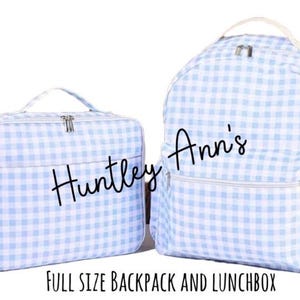 May include: A light blue and white gingham-patterned backpack and matching lunchbox. The backpack has a front pocket and side pockets. The lunchbox has a handle and a zipper closure. The text "Huntley Ann's" is on both items. The text "FULL SIZE BACKPACK AND LUNCHBOX" is at the bottom.