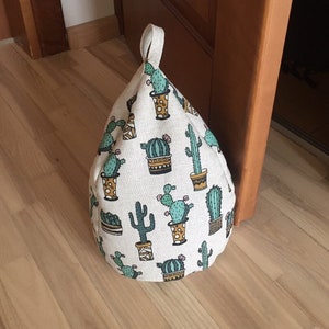 May include: A beige doorstop shaped like a pyramid with a green cactus print. The doorstop is made of fabric and has a loop handle.