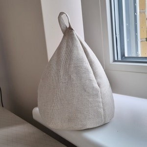 May include: A beige linen doorstop in the shape of a cone with a loop handle.