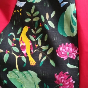 May include: Black fabric with a green, yellow, and pink floral pattern. The fabric features a yellow bird with pink and red accents perched on a branch with green leaves. The fabric is bordered by a solid red fabric.