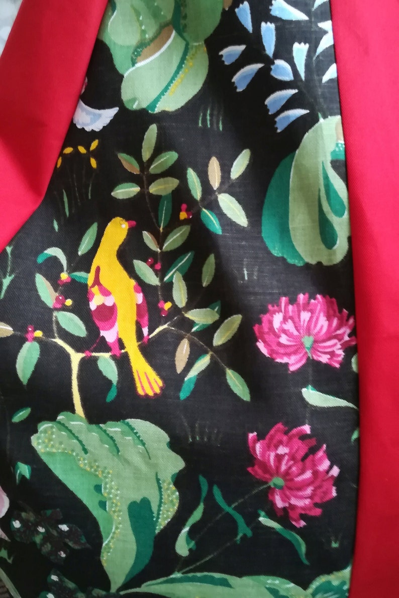 May include: Black fabric with a green, yellow, and pink floral pattern. The fabric features a yellow bird with pink and red accents perched on a branch with green leaves. The fabric is bordered by a solid red fabric.