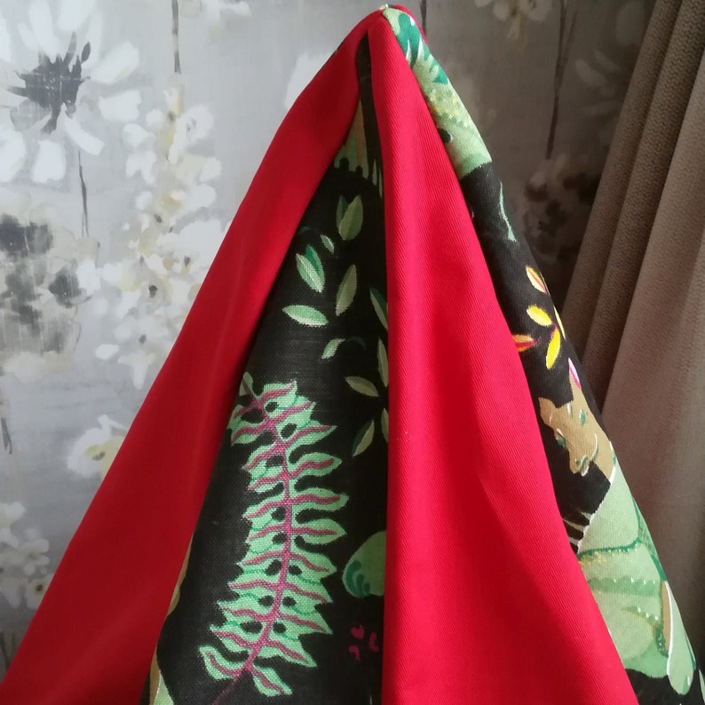 May include: A red, black, and green fabric with a leafy pattern. The fabric is folded into a triangular shape.