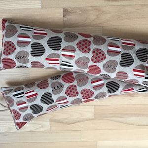 May include: Two doorstop pillows with a beige background and a pattern of red, black, and white hearts. The hearts have different patterns, including polka dots, stripes, and a black and white geometric design.