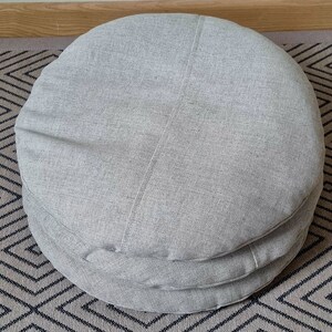Op de afbeelding: Een stapel van drie ronde grijze stoffen kussens. De kussens zijn gemaakt van een zachte, gestructureerde stof en zijn perfect om elke kamer een vleugje comfort te geven.