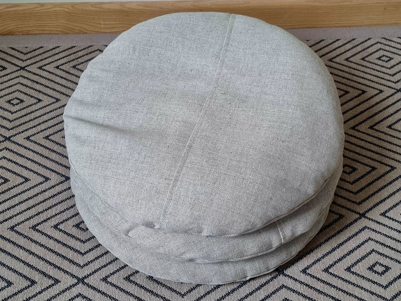 Op de afbeelding: Een stapel van drie ronde grijze stoffen kussens. De kussens zijn gemaakt van een zachte, gestructureerde stof en zijn perfect om elke kamer een vleugje comfort te geven.