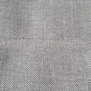 Op de afbeelding: Close-up van een lichtgrijze geweven stof met een subtiele textuur. De stof heeft een gladde, gelijkmatige weving en een licht ruw gevoel.