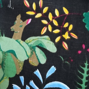 May include: A black fabric with a hand-painted design featuring a deer, leaves, and flowers. The deer is brown with green leaves around it. The leaves are yellow and green with red stems. The flowers are blue and pink.