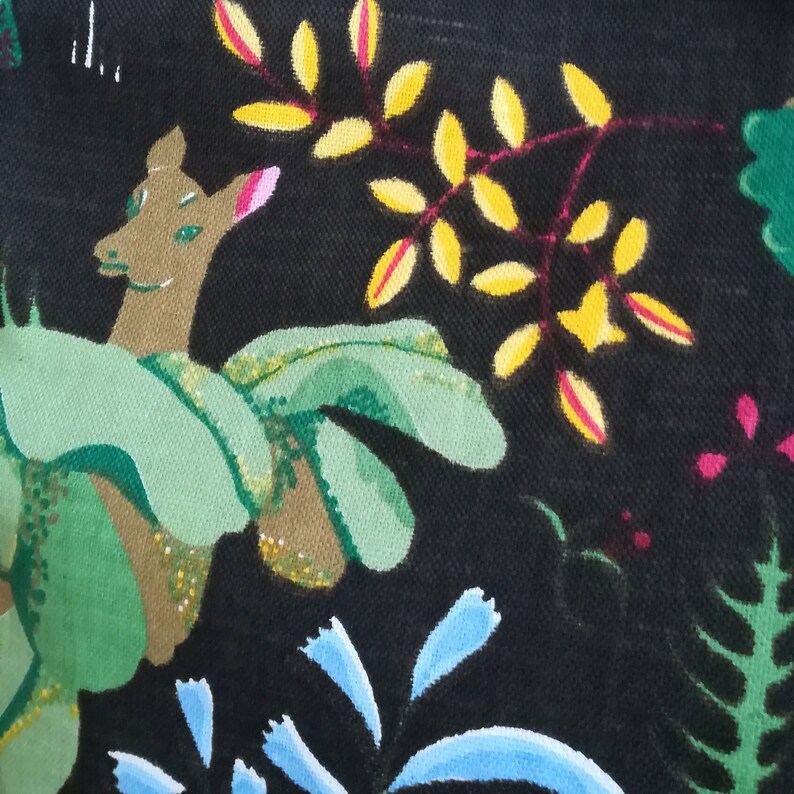 May include: A black fabric with a hand-painted design featuring a deer, leaves, and flowers. The deer is brown with green leaves around it. The leaves are yellow and green with red stems. The flowers are blue and pink.