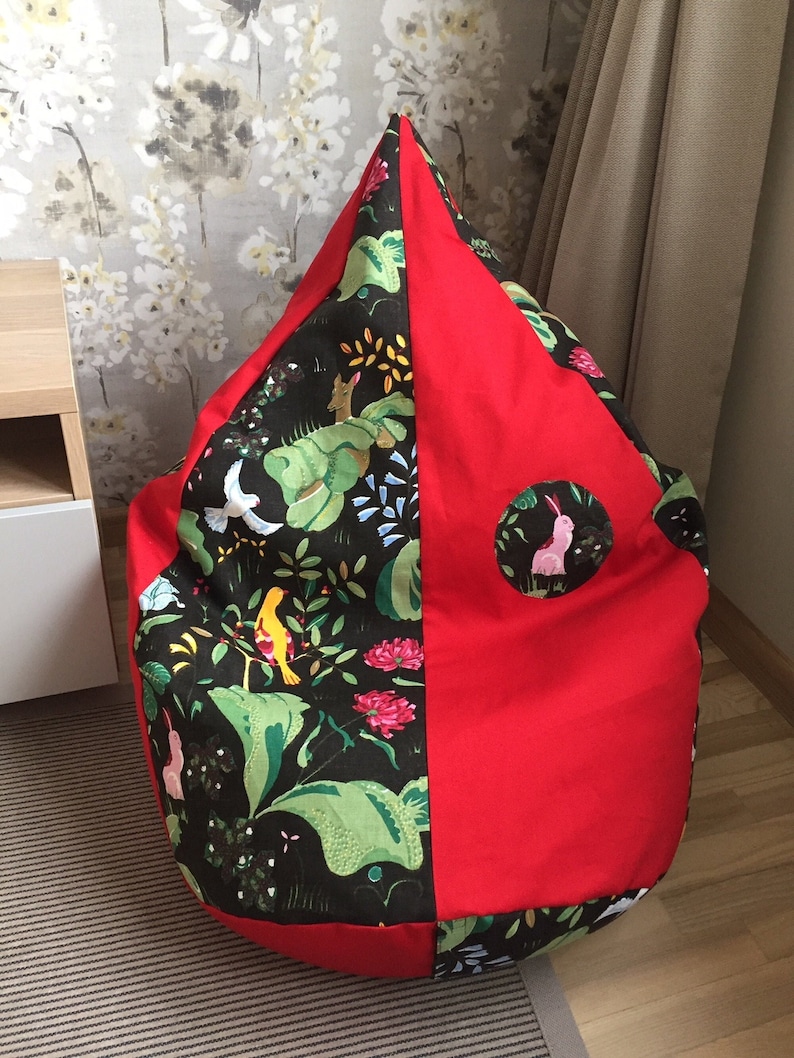 May include: A large, red and green beanbag chair with a floral pattern. The chair is shaped like a teardrop and has a small, round window on the red side.