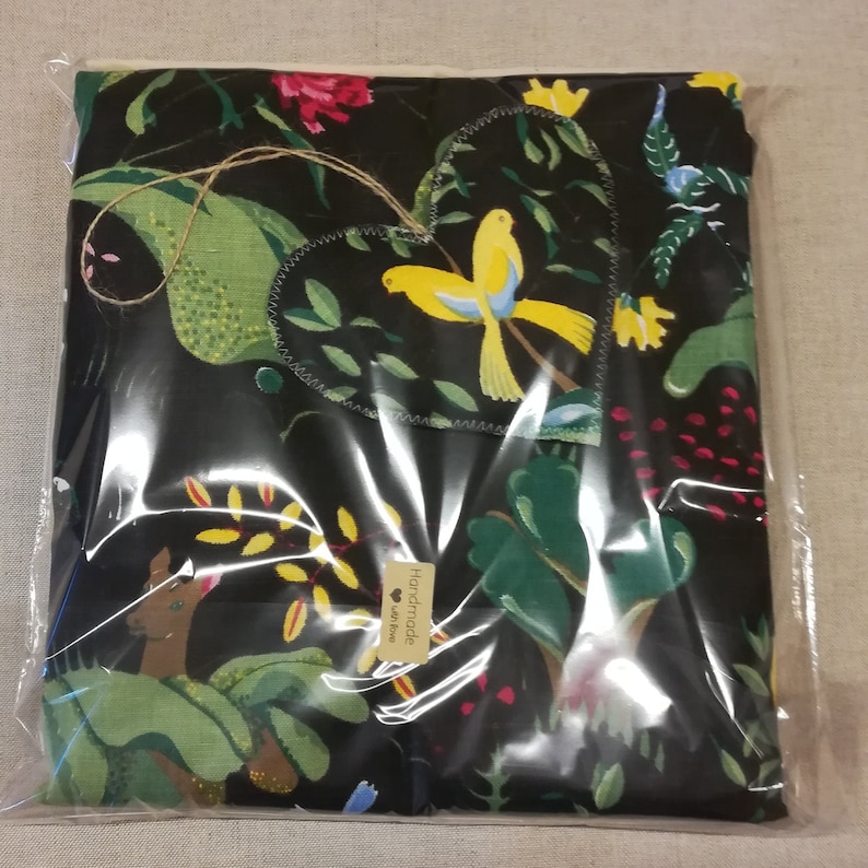 May include: A black fabric with a green, yellow, and red floral pattern. A heart-shaped tag with two yellow birds is attached to the fabric. The tag says "Handmade with Love".