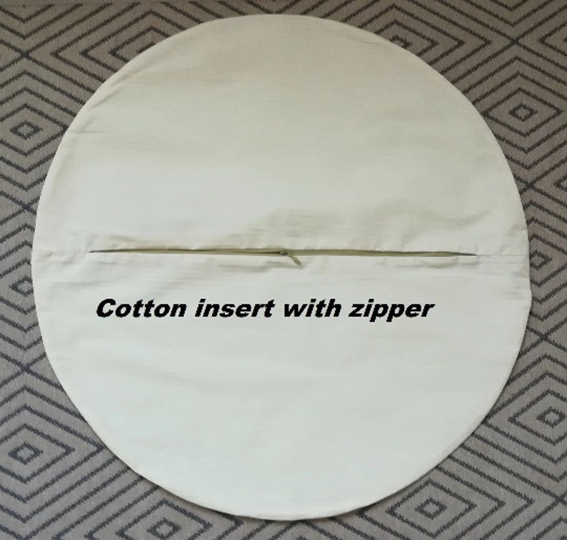 Op de afbeelding: Een ronde, witte katoenen kussenhoes met een ritsopening. De tekst "Cotton insert with zipper" is op de hoes gedrukt.