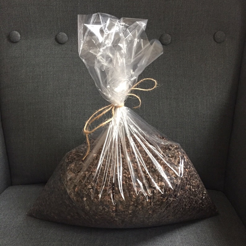 A close up of a clear transparent plastic bag filled with natural brown buckwheat hulls tied neatly with a rustic jute twine string