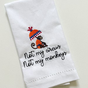 May include: White tea towel with an embroidered monkey holding an umbrella and the text "Not my circus, not my monkeys."