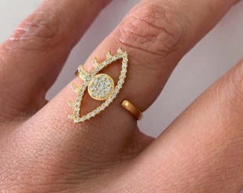 May include: Gold ring with a clear crystal eye design. The eye is surrounded by smaller crystals.