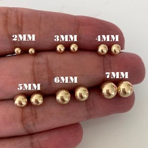 May include: A set of 10 gold ball stud earrings in various sizes, ranging from 2mm to 7mm. The earrings are displayed on a hand, with each size labeled.