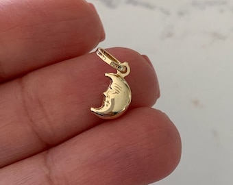 May include: A gold crescent moon charm pendant. The moon has a face on it.