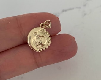 May include: A gold pendant featuring a sun and moon design. The sun has a face and the moon is a crescent shape.