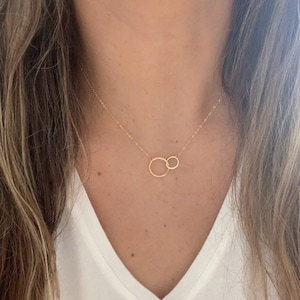 May include: A gold chain necklace with two interlocking circles as a pendant.