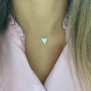 Puede incluir: Un collar de plata con un peque&ntilde;o colgante en forma de coraz&oacute;n. El colgante est&aacute; cubierto de peque&ntilde;as piedras brillantes.