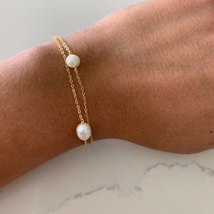 May include: A delicate gold chain bracelet with two white pearls. The bracelet is layered with two chains.