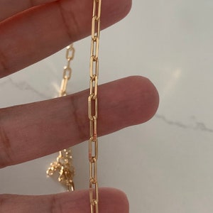 May include: A gold chain necklace with a delicate, flat, rectangular link design.