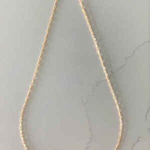 May include: A gold chain necklace with a delicate, linked chain design. The chain is made of small, rectangular links.