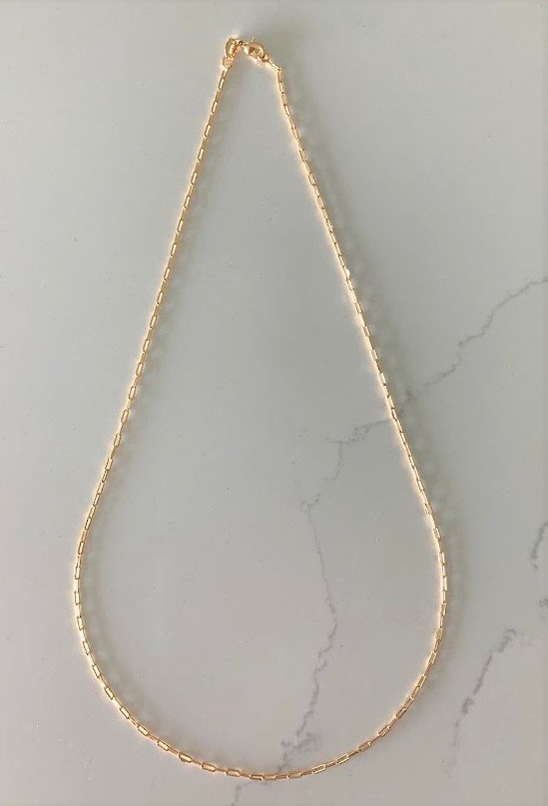 May include: A gold chain necklace with a delicate, linked chain design. The chain is made of small, rectangular links.