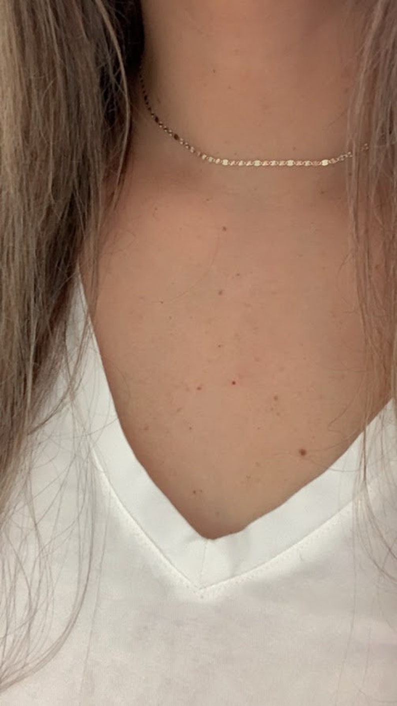 May include: A close-up of a person's neck wearing a delicate gold chain necklace.