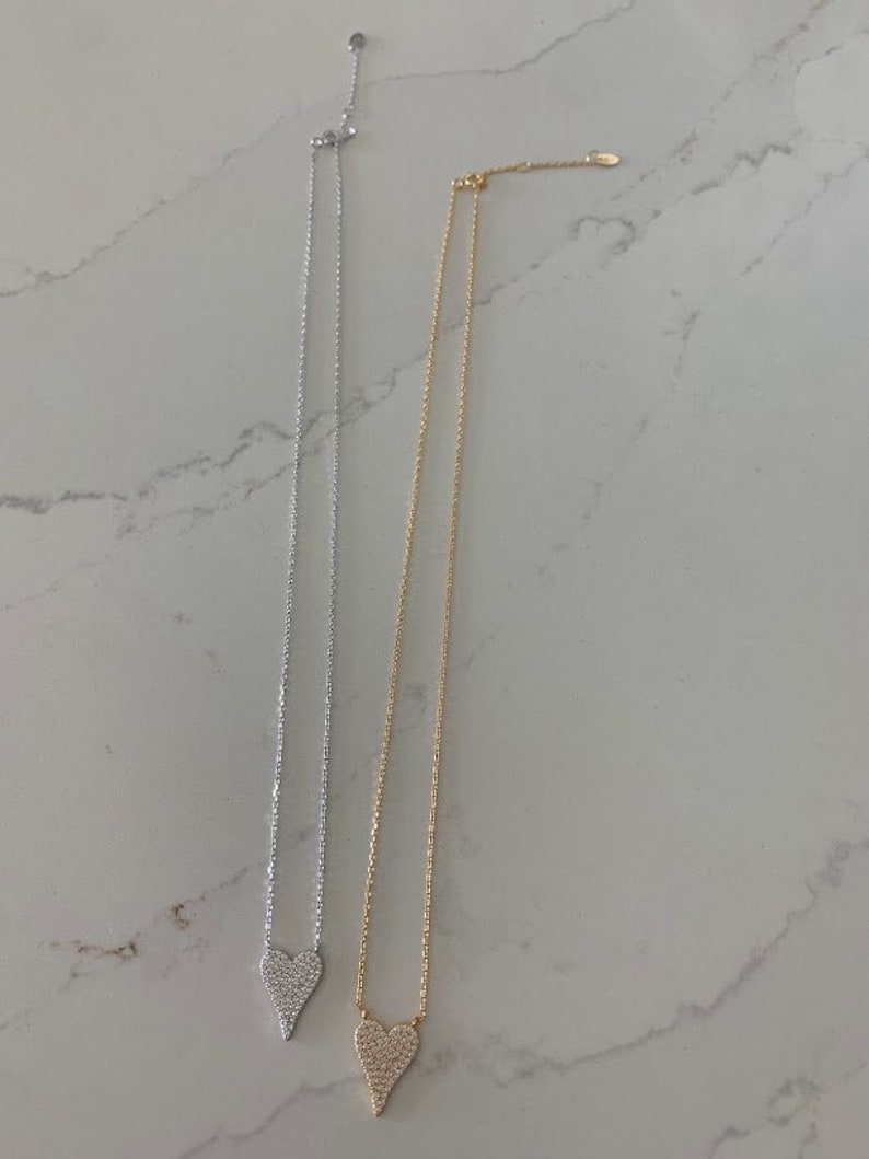Puede incluir: Dos delicados collares con un colgante de coraz&oacute;n. El colgante de coraz&oacute;n est&aacute; cubierto de peque&ntilde;as piedras brillantes. Un collar es plateado y el otro es dorado.