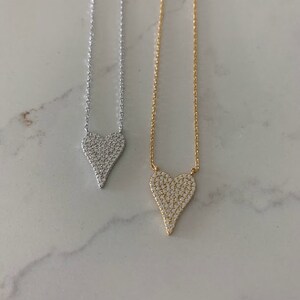 Puede incluir: Dos delicados collares con colgantes en forma de coraz&oacute;n. Los colgantes est&aacute;n cubiertos de piedras brillantes transparentes. Un collar tiene una cadena plateada y el otro una cadena dorada.