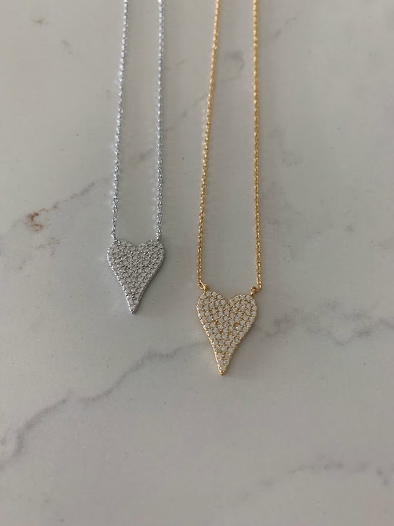 Puede incluir: Dos delicados collares con colgantes en forma de coraz&oacute;n. Los colgantes est&aacute;n cubiertos de piedras brillantes transparentes. Un collar tiene una cadena plateada y el otro una cadena dorada.