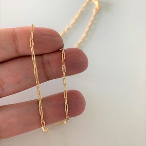 May include: A gold chain necklace with a delicate, linked chain design. The chain is made of small, rectangular links.