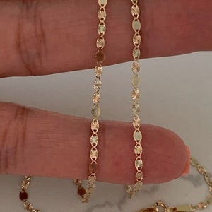 May include: A gold chain necklace with a delicate, patterned design. The chain is made of small, oval-shaped links with a diamond-shaped pattern.