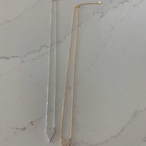 Puede incluir: Dos collares de plata y oro con un colgante de coraz&oacute;n. Cada coraz&oacute;n est&aacute; cubierto de peque&ntilde;as piedras transparentes.